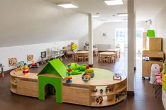 Sala żłobka z zielonym domkiem, zabawkami i stolikami dla dzieci